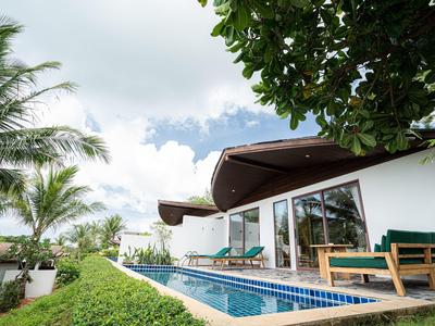 Moderner Bungalow mit Glasfront, Terrasse, Pool, umgeben von Palmen und grünem Pflanzenwuchs.