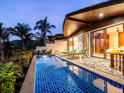 Moderner Bungalow mit langem blauen Pool, Patio und Palmen bei Dämmerung.