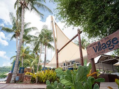 Tropische Strandbar mit Palmen, weißen Sonnensegeln und grünem Pflanzenbewuchs bei blauem Himmel.