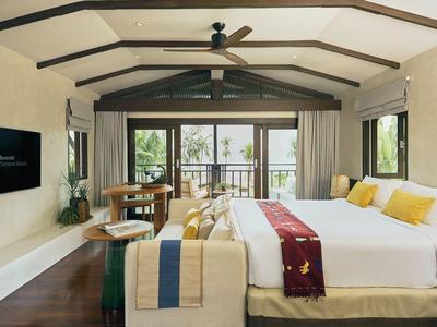 Moderne hotelkamer met groot bed, bank, flatscreen-tv en balkon met uitzicht op palmbomen.