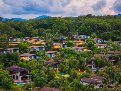 Mehrere Bungalows in einem üppig grünen Waldgebiet mit Bergen im Hintergrund.
