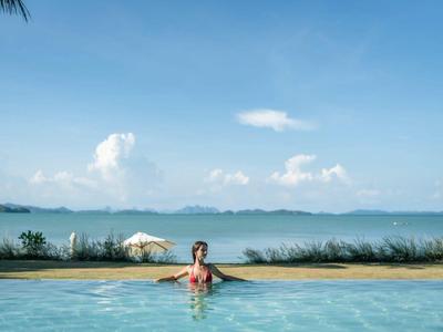 Person entspannt in einem Pool mit Blick auf Meer und bewölkten Himmel.