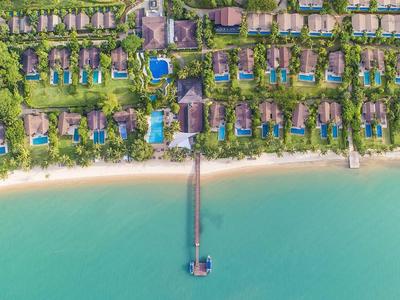 Luftaufnahme eines Resorts mit Villen, Poolbereichen und einem langen Steg am Strand.