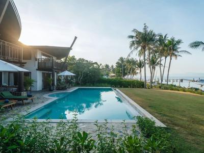 Modern zwembad naast een hotel met uitzicht op zee en palmbomen bij zonsondergang.