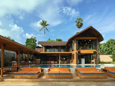 Moderne hotelzwembad met ligstoelen en houten paviljoen onder een blauwe lucht.