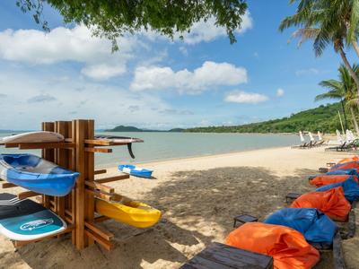 Ein tropischer Sandstrand mit Kajaks und bunten Sitzsäcken unter Palmen und blauem Himmel.
