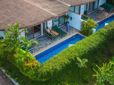 Blick von oben auf ein Hotel mit Schwimmbecken, Sonnenliegen und grüner Hecke