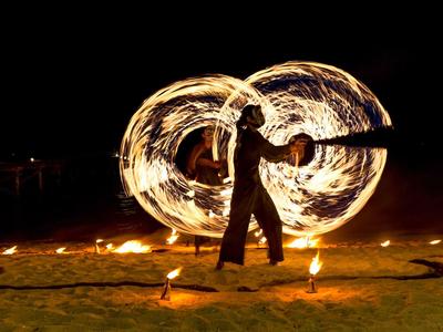 Ein Feuerspucker erzeugt mit brennenden Fackeln helle, kreisförmige Lichtspuren in der Nacht.