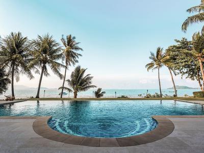 Ein runder Pool mit Palmen an einem ruhigen Strand und klarem Himmel im Hintergrund.