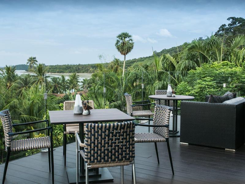 Taras z krzesłami i stołami otoczony tropikalną roślinnością z widokiem na wzgórza.