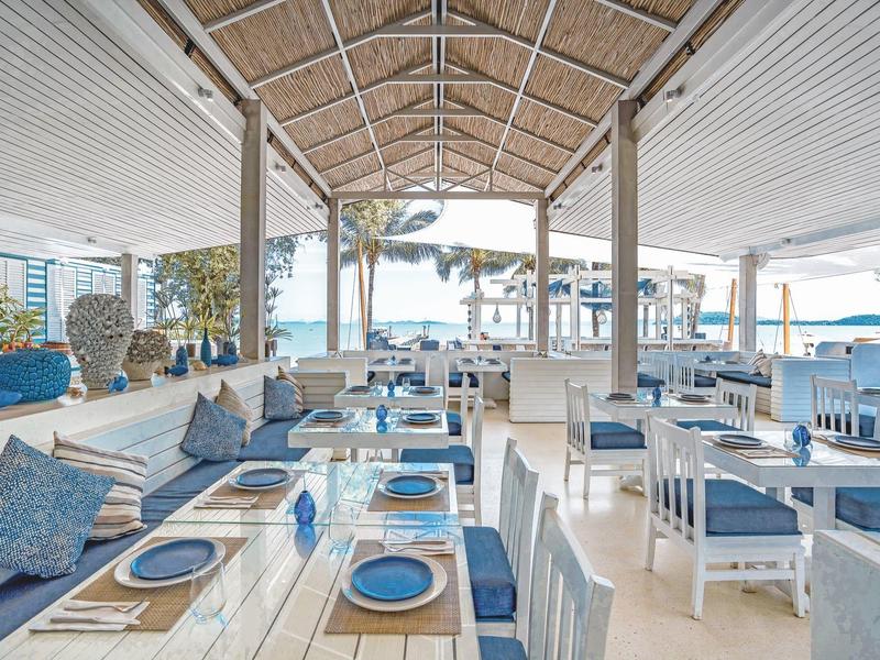 Otwarta, jasno urządzona przestrzeń restauracyjna z widokiem na morze i nakrytymi stolikami.