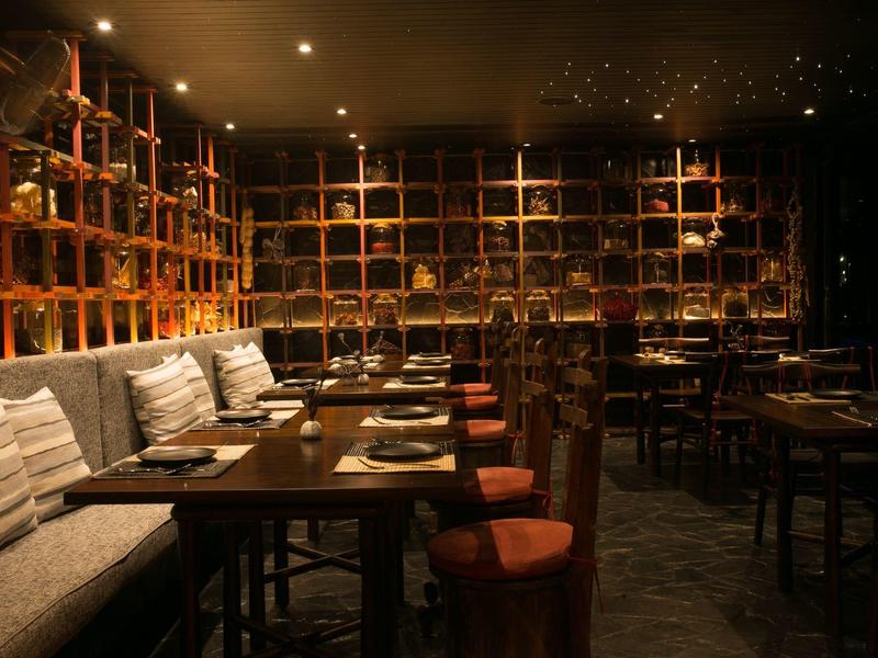 Przytulna restauracja z drewnianymi stołami, krzesłami i ciepłym, przyćmionym światłem.