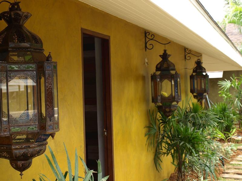 Trzy dekoracyjne lampiony wiszą na żółtej ścianie domu obok wejścia i zielonych roślin.