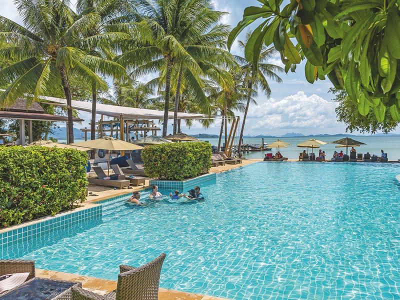 Basen na zewnątrz z leżakami, palmami i widokiem na morze przy czystym niebie.