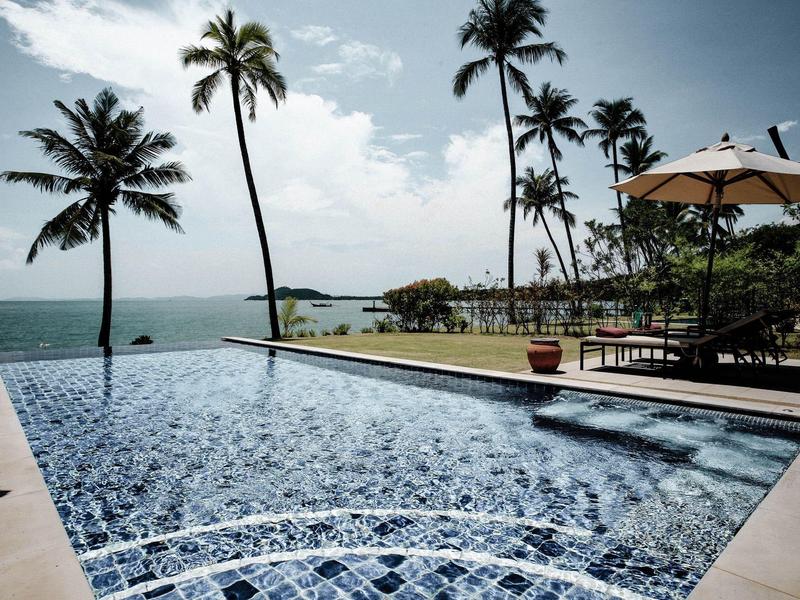 Basen typu infinity z palmami i widokiem na ocean pod pochmurnym niebem.