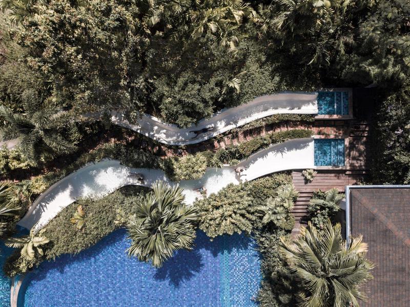 Dwa zjeżdżalnie wodne przechodzą przez zieloną roślinność do niebieskiego basenu w ośrodku hotelowym.