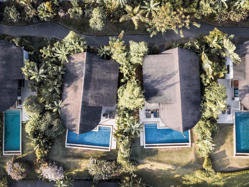 Widok z lotu ptaka na dwa sąsiednie domy z basenami i bujnymi ogrodami.