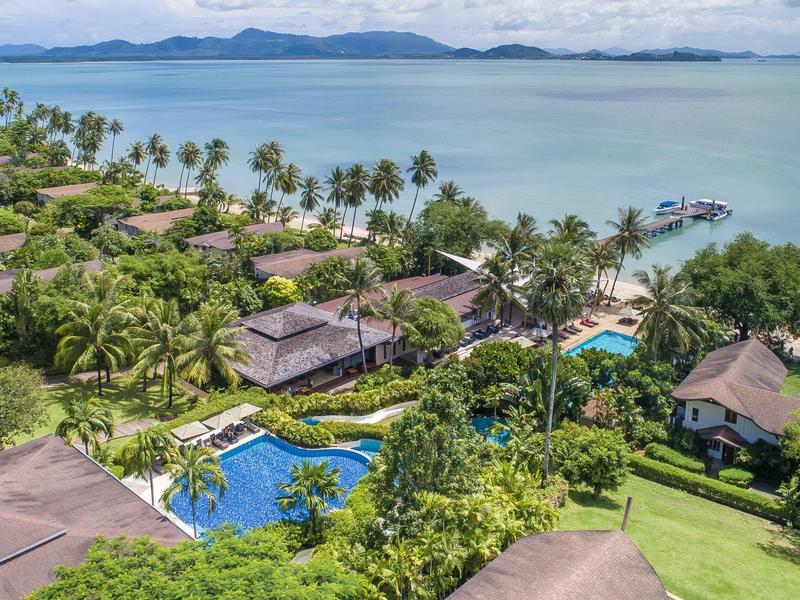 Widok na ośrodek z basenem, tropikalnymi ogrodami i morzem z wyspami w tle.