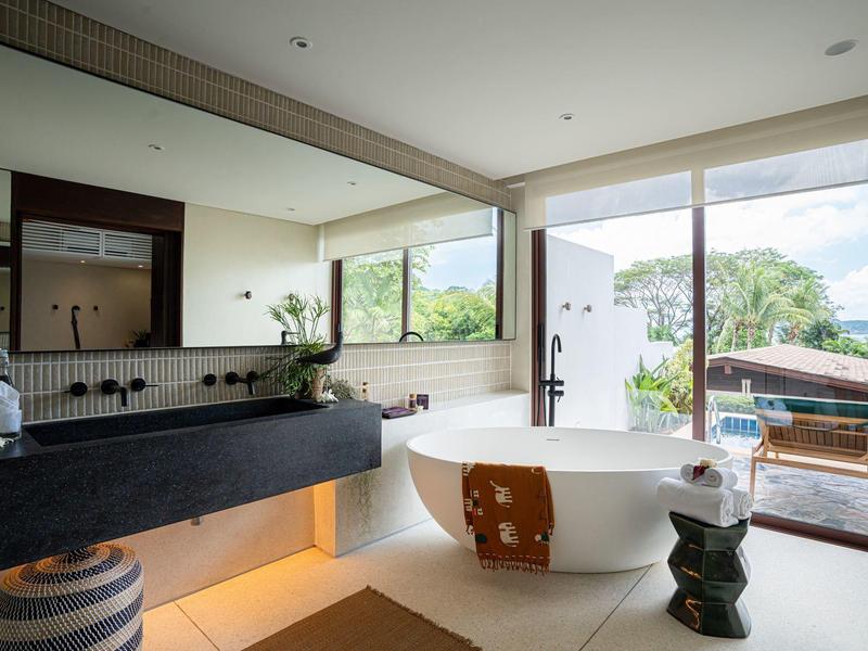 Nowoczesna łazienka hotelowa z wolnostojącą wanną, dużym lustrem i widokiem na taras i góry.