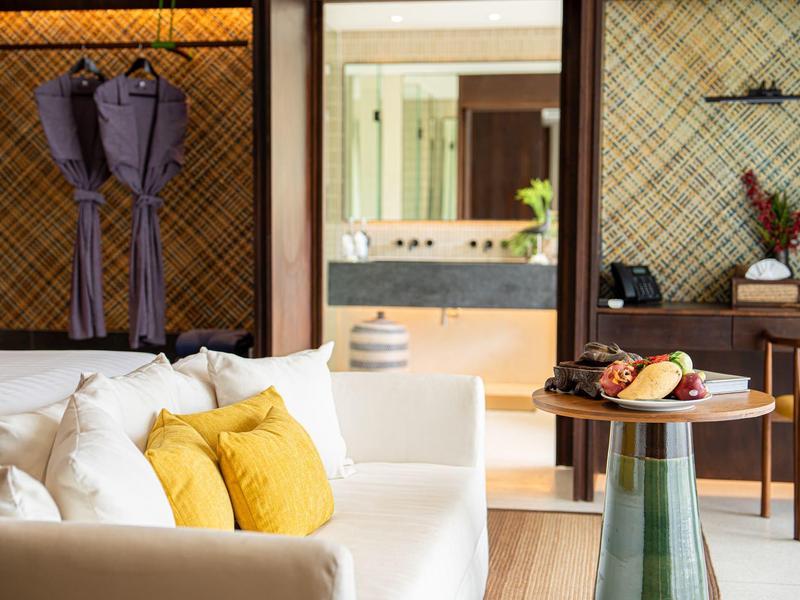 Przytulny salon z białą sofą, żółtymi poduszkami i stołem jadalnym z miską owoców.