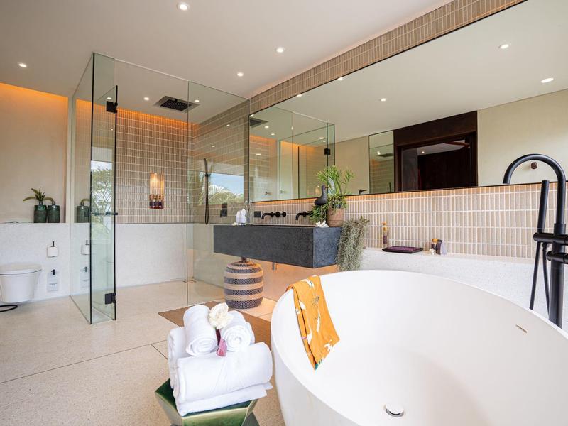 Nowoczesna łazienka z wolnostojącą wanną, umywalką i dużą ścianą lustra.