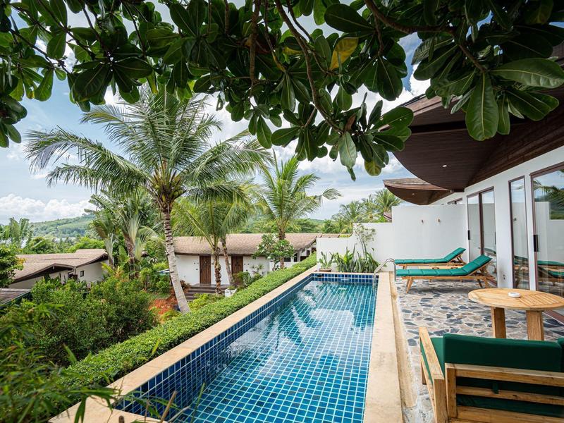 Nowoczesny basen z niebieskimi płytkami obok tarasu i tropikalnej roślinności.