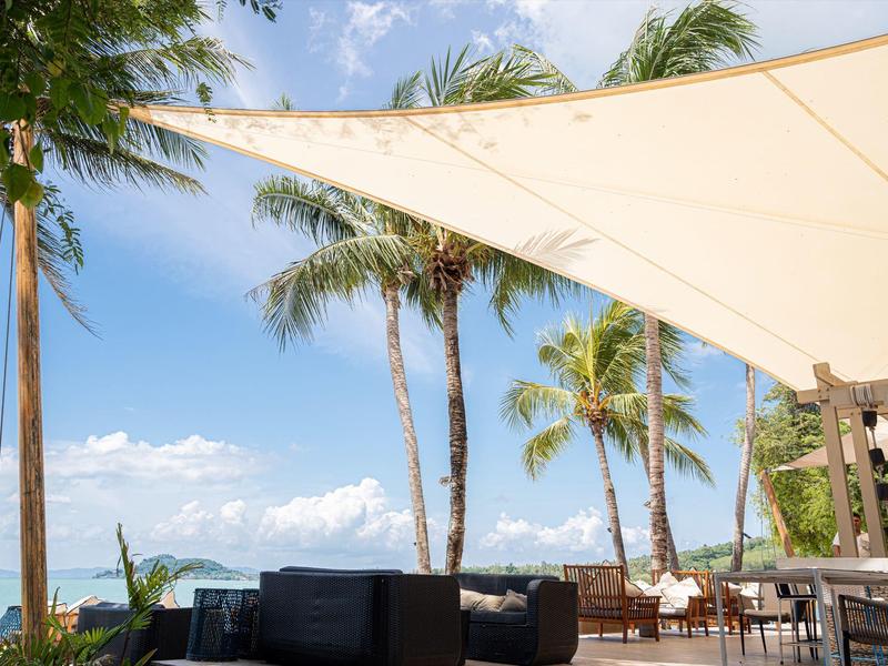 Taras z żaglem przeciwsłonecznym, palmami i miejscem do siedzenia pod czystym niebem nad morzem