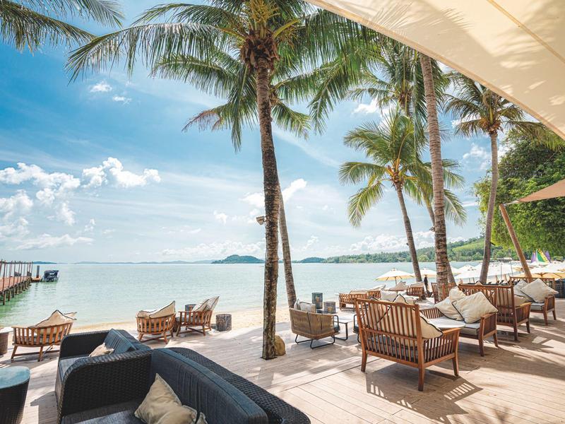 Relaksujący taras na plaży z leżakami i palmami nad morzem pod niebieskim niebem.