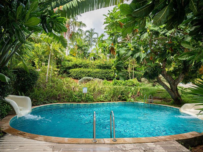 Okrągły basen z wodospadem, otoczony gęstą tropikalną roślinnością i palmami.