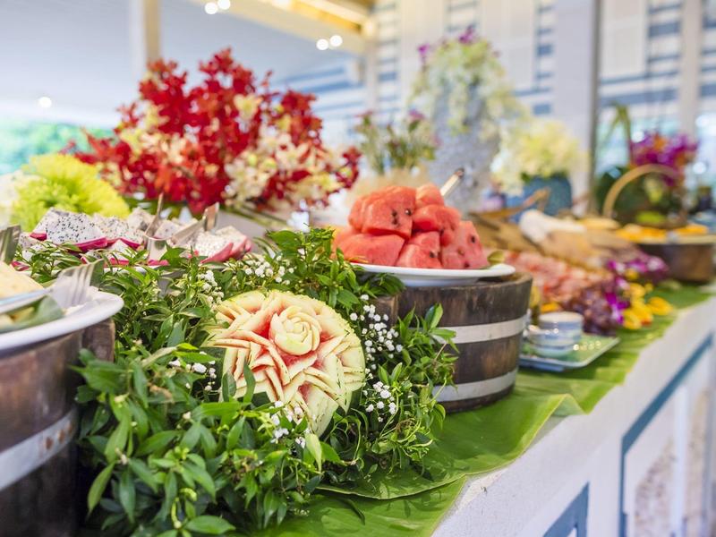 Kolorowy bufet z różnorodnymi owocami i dekoracyjnymi roślinami w jasnym pomieszczeniu.