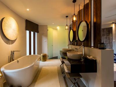 Moderne badkamer met vrijstaand bad en twee ronde spiegels aan donkere houten wand.