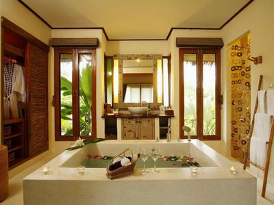 Licht badkamer met groot bad, ramen en houten meubels in een ontspannende sfeer.