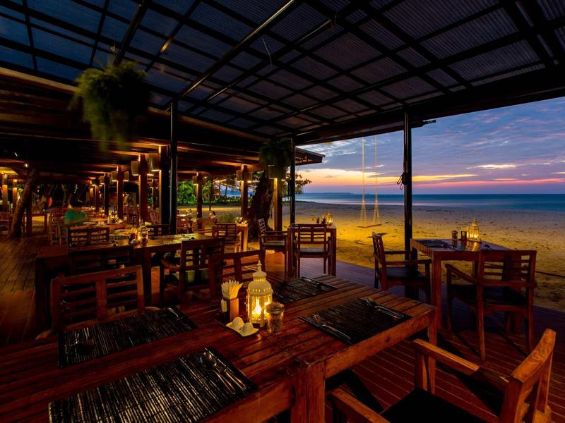 Gezellig strandrestaurant bij zonsondergang met houten tafels en uitzicht op zee.