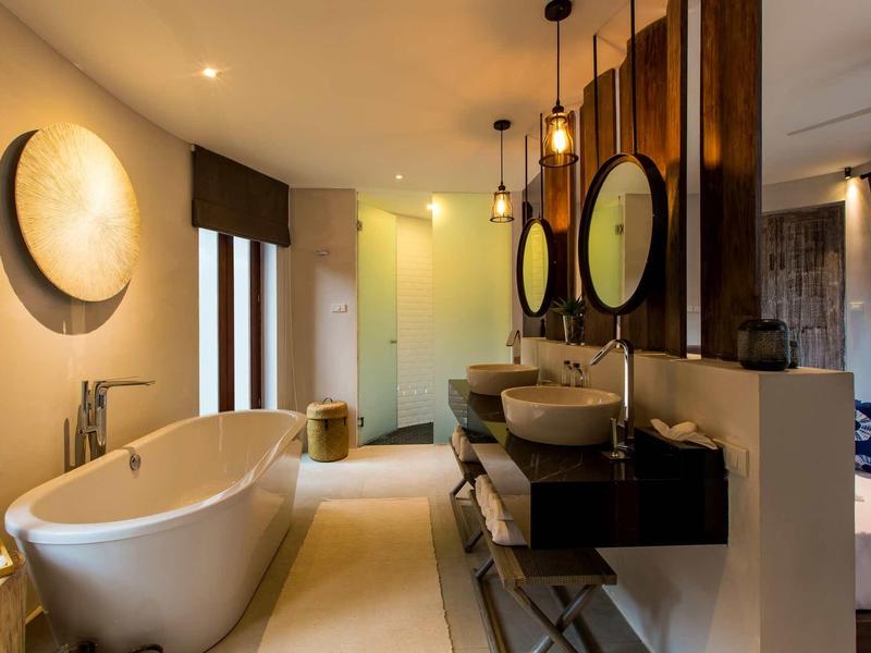 Moderne badkamer met vrijstaand bad en twee ronde spiegels aan donkere houten wand.