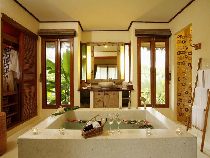 Licht badkamer met groot bad, ramen en houten meubels in een ontspannende sfeer.