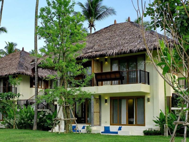 Twee gele vakantiehuizen met bruine daken omgeven door groen landschap en bomen.