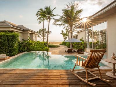 Moderner Pool mit Holzdeck und Schaukelstuhl neben tropischen Palmen bei Sonnenuntergang.