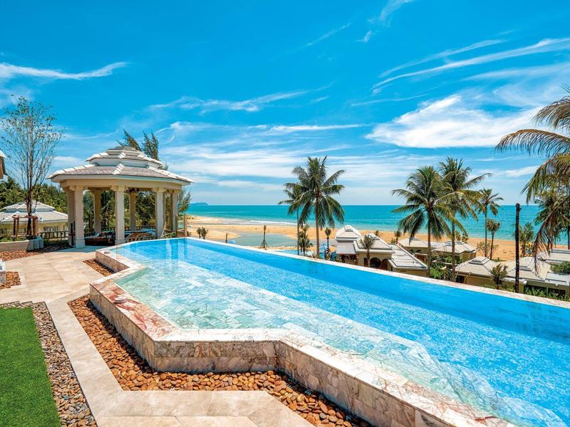 Piscine de luxe avec vue sur la plage et les palmiers sous un ciel bleu.