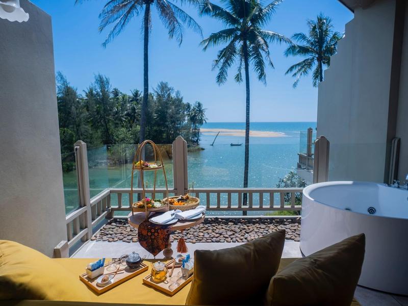 Balcon avec jacuzzi, coussins et vue sur la mer avec des palmiers.