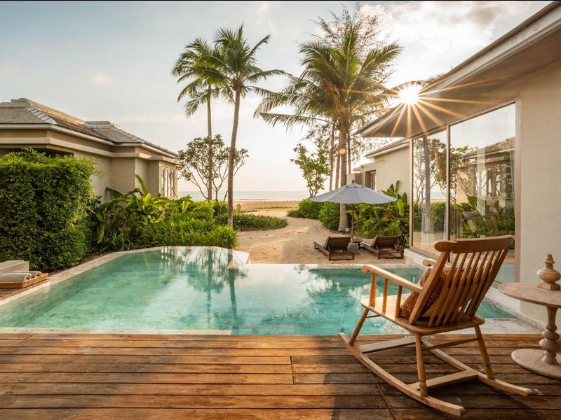 Espace piscine moderne avec terrasse en bois, chaise longue et vue sur les palmiers et la mer.