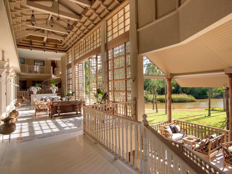 Balcon d'hôtel lumineux avec sol en bois, tables et chaises, vue sur un jardin vert.