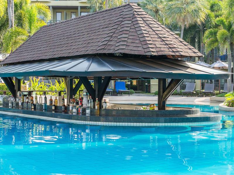 Basen z barem pod zacienionym dachem pawilonu, otoczony palmami.