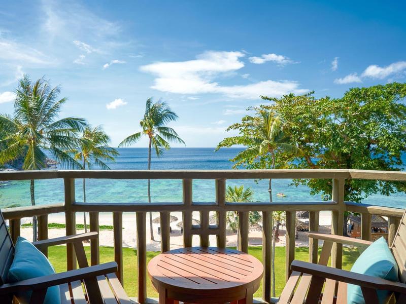 Widok z balkonu z drewnianymi meblami na plażę z palmami i niebieskie niebo