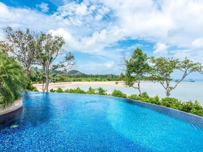 Piscina a sfioro con vista sulla spiaggia e sull'oceano sotto un cielo azzurro.