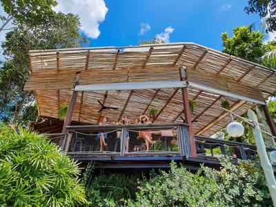 Padiglione moderno con ringhiera in vetro circondato da alberi verdi rigogliosi sotto il cielo blu