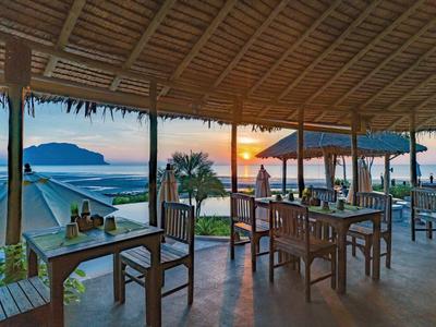 Otwarta restauracja z drewnianymi meblami i widokiem na zachód słońca na plaży.