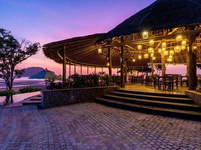 Ristorante all'aperto con vista sul mare al tramonto, illuminato da luci calde.