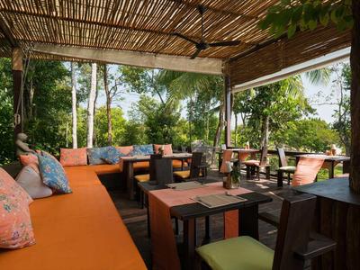 Zadaszona przestrzeń wypoczynkowa z poduszkami i stołami w naturalnym otoczeniu.