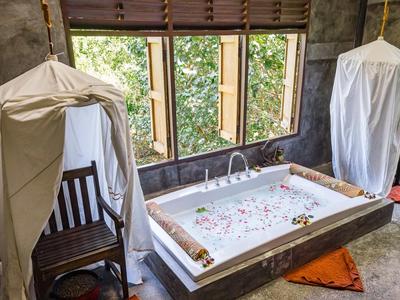 Un bagno di lusso con una vasca da bagno piena, sedia di legno e tende alle finestre.