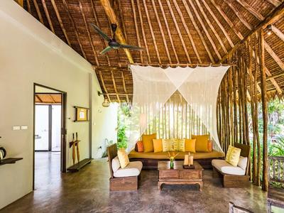 Accogliente lounge con zanzariera sotto un tetto di paglia, circondato da vegetazione tropicale.